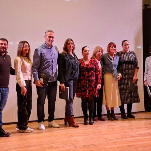 Group of ten people on a stage posing with award folders during a ceremony on a projector-backed backdrop.