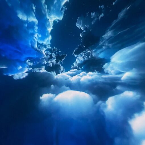 Blue sky with scattered white clouds and a deep blue gradient, resembling a view through an opening in the clouds with a few stars.