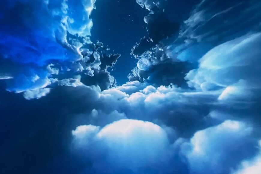 Blue sky with scattered white clouds and a deep blue gradient, resembling a view through an opening in the clouds with a few stars.
