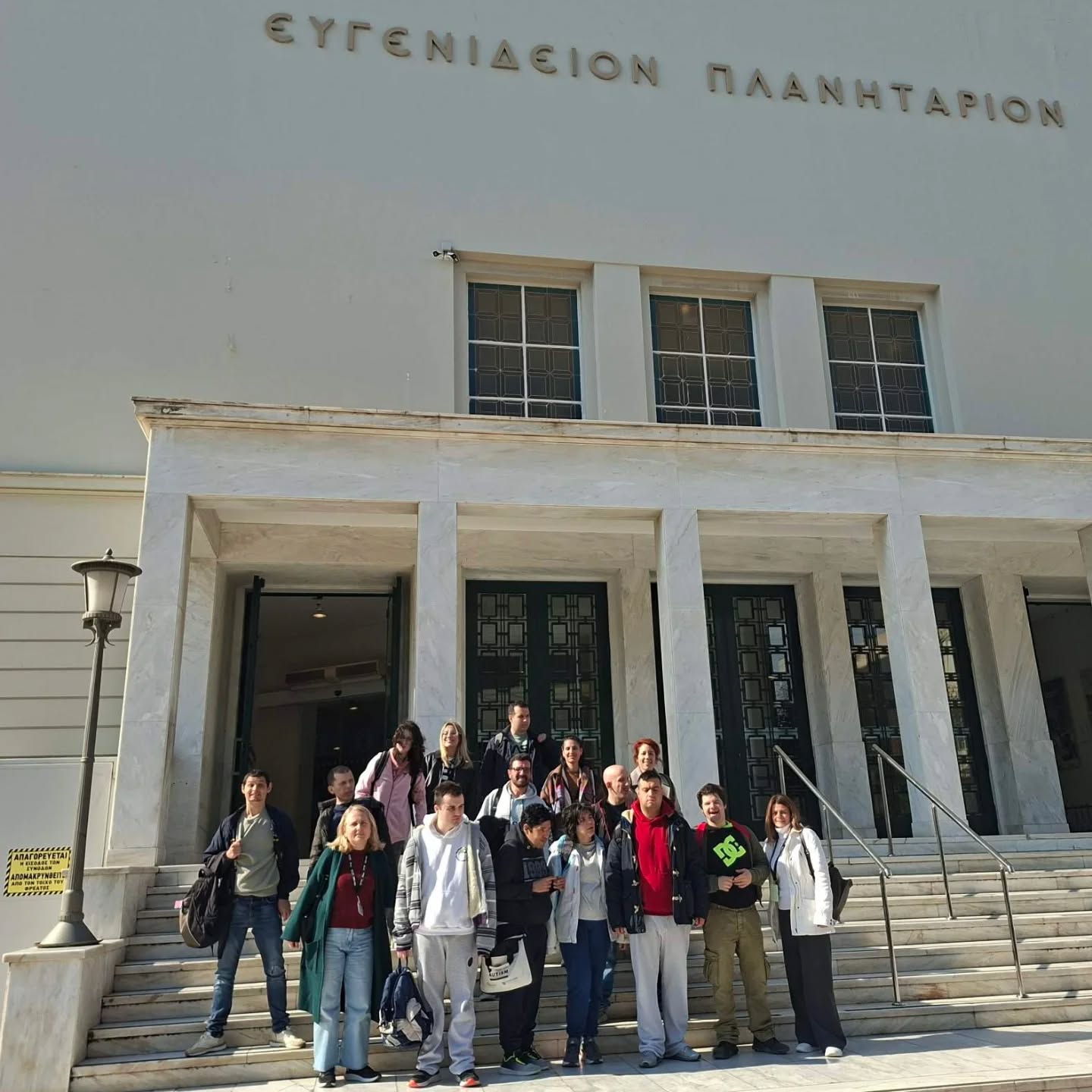 Group of students posing on marble steps in front of a light-colored building with Greek lettering above the entrance