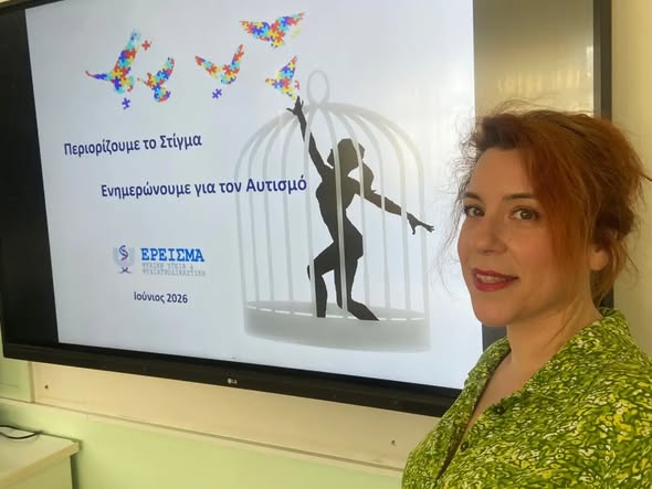 Woman in a green patterned blouse stands beside a presentation slide about autism awareness, featuring colorful butterflies and a silhouette in a cage.